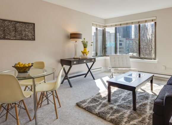 A modern apartment living room with a glass-top dining table, neutral decor, and clean lines in a small space