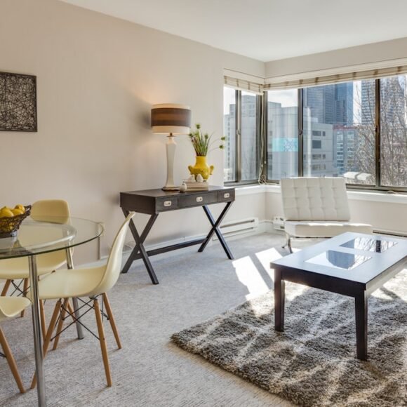 A modern apartment living room with a glass-top dining table, neutral decor, and clean lines in a small space