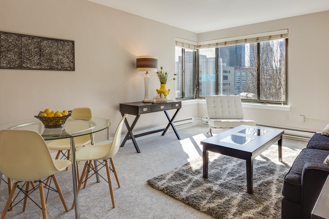 A modern apartment living room with a glass-top dining table, neutral decor, and clean lines in a small space