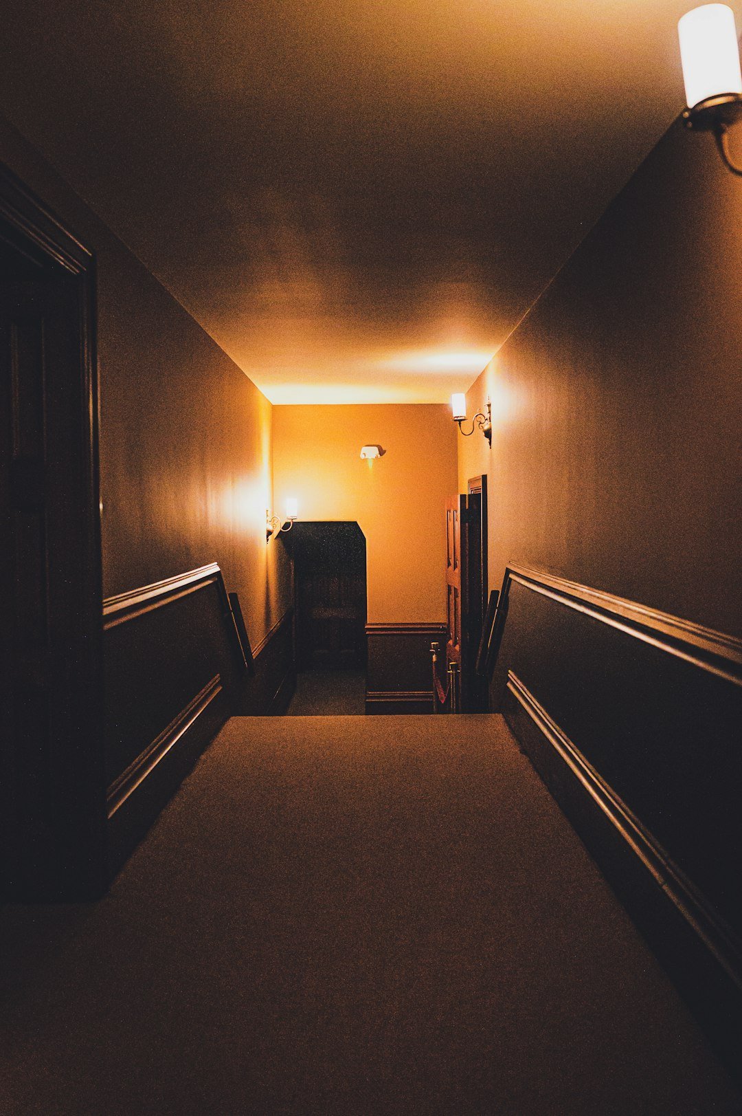 Dimly lit apartment hallway with warm ambient lighting leading to another room