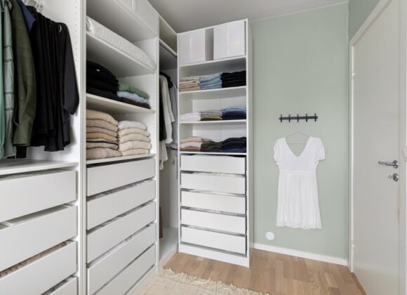 A small walk-in closet neatly organized with white drawers, hanging clothes, and labeled storage bins