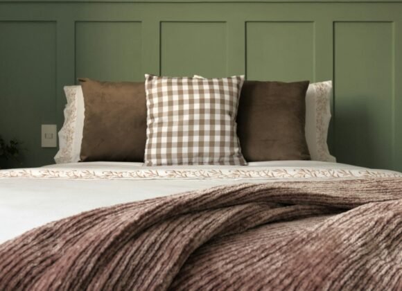 Bed layered with a folded knit blanket and mixed cushions