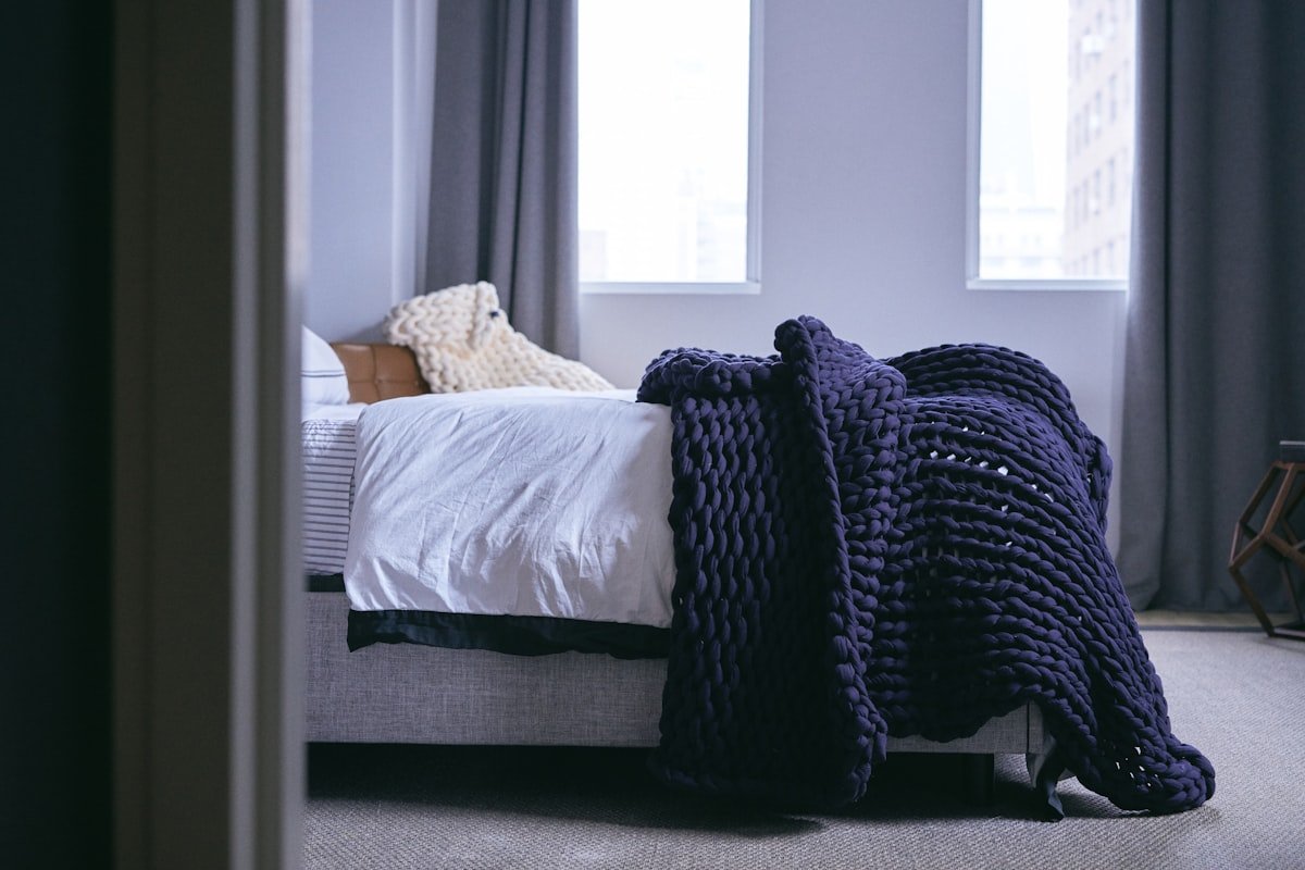 Heavy knit blanket folded across a bed beside a window