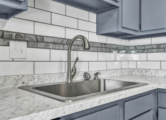 White subway tile backsplash above a marble look counter with a stainless steel sink and gray kitchen cabinets