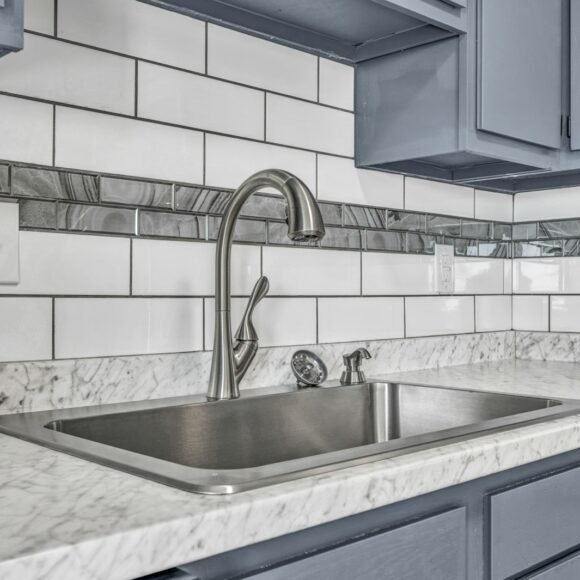 White subway tile backsplash above a marble look counter with a stainless steel sink and gray kitchen cabinets