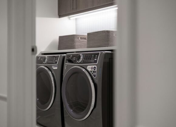 A laundry room with a matching washer and dryer side by side under a shelf