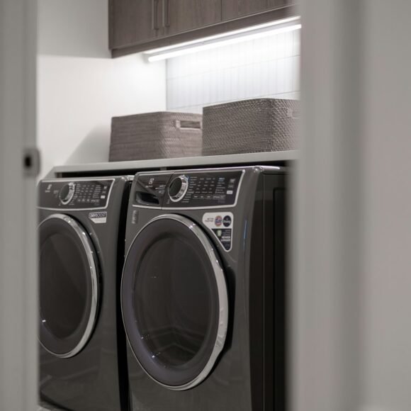 A laundry room with a matching washer and dryer side by side under a shelf