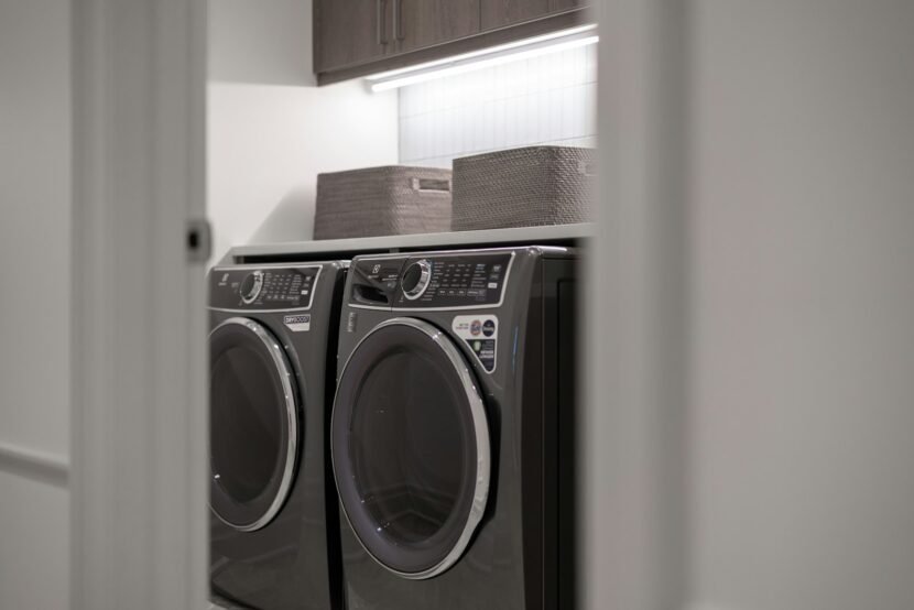A laundry room with a matching washer and dryer side by side under a shelf